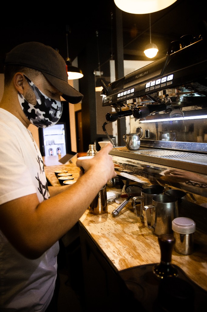 Barista pouring latte art behind espresso bar with warm pendant lighting