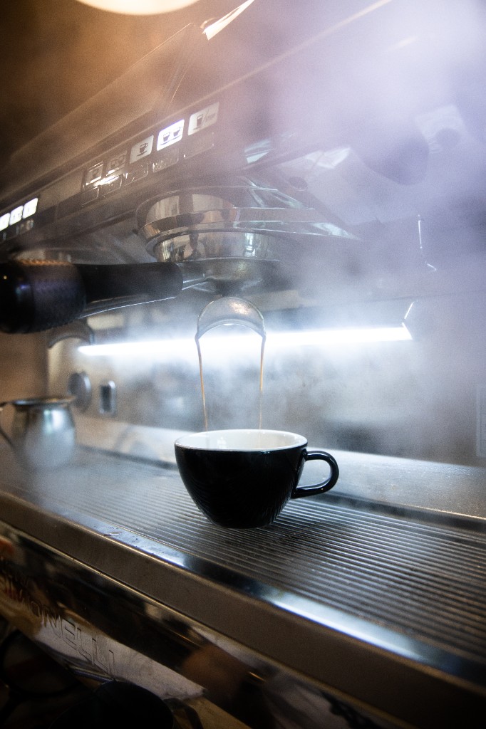 Espresso extracting into black cup with steam and machine detail