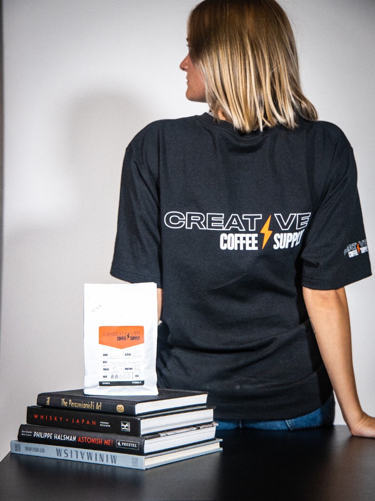 Creative Coffee Supply bag on stacked books with branded shirt