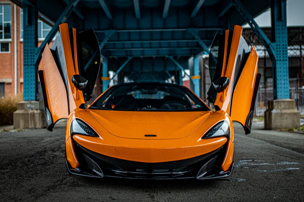 Front symmetry shot of orange McLaren with doors open beneath an overpass