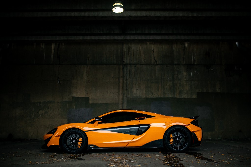 Orange McLaren side profile parked under an underpass in wet conditions