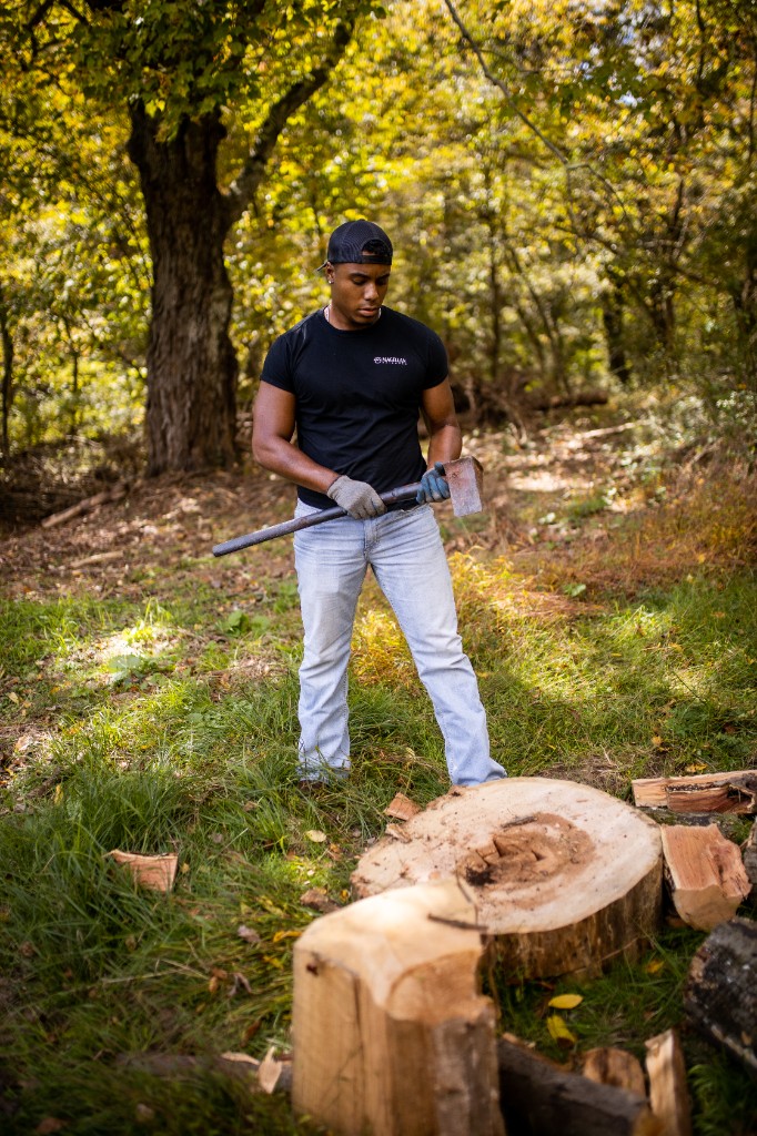 Tony Evans Jr. with axe at woodpile in forest clearing