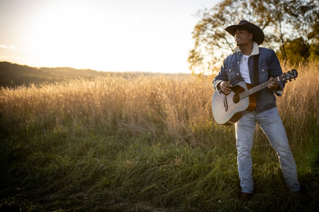 Tony Evans Jr. playing acoustic guitar in a golden field at sunset