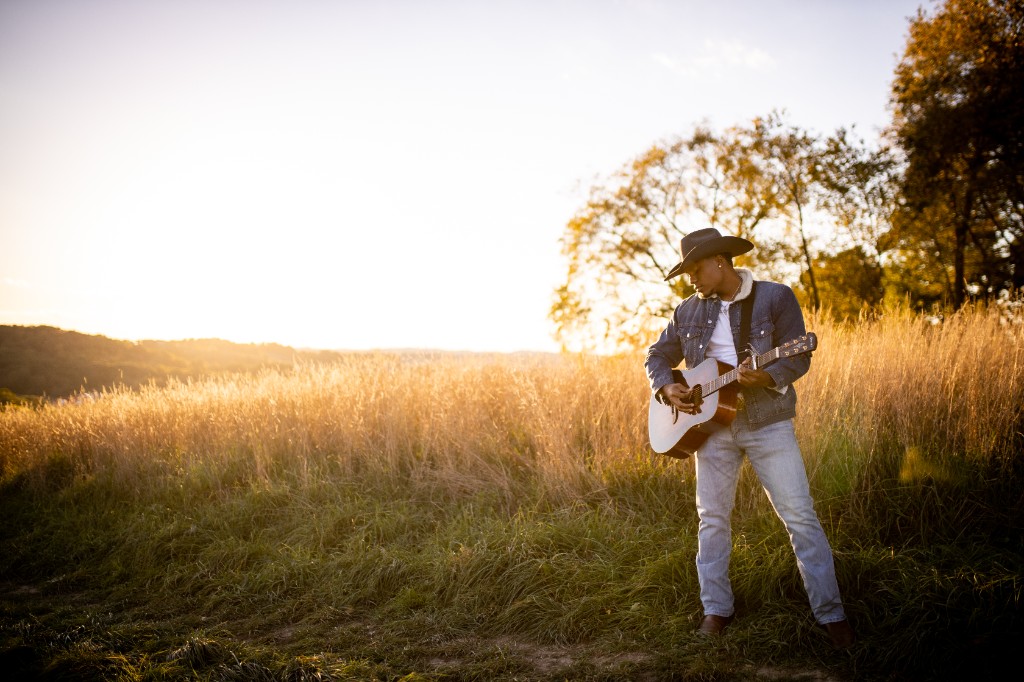 Tony Evans Jr. playing guitar in golden field with open sky