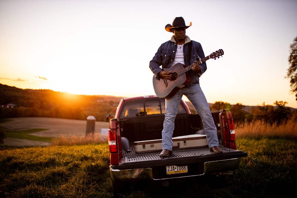 Tony Evans Jr. standing in pickup truck bed playing guitar at golden hour