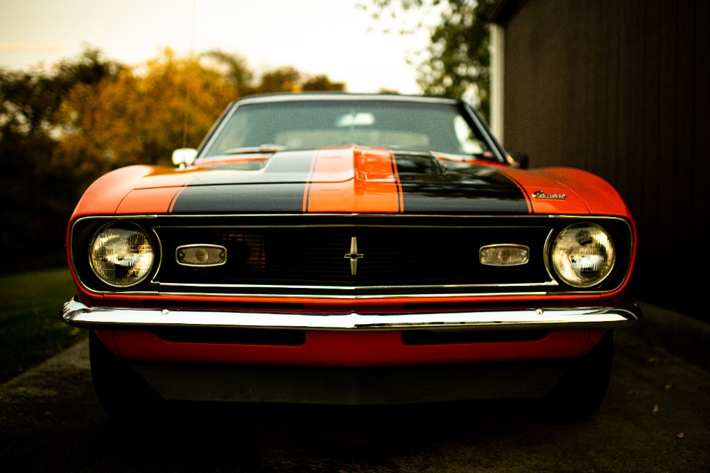 Front view of orange first-generation Chevrolet Camaro with black hood stripes and chrome bumper