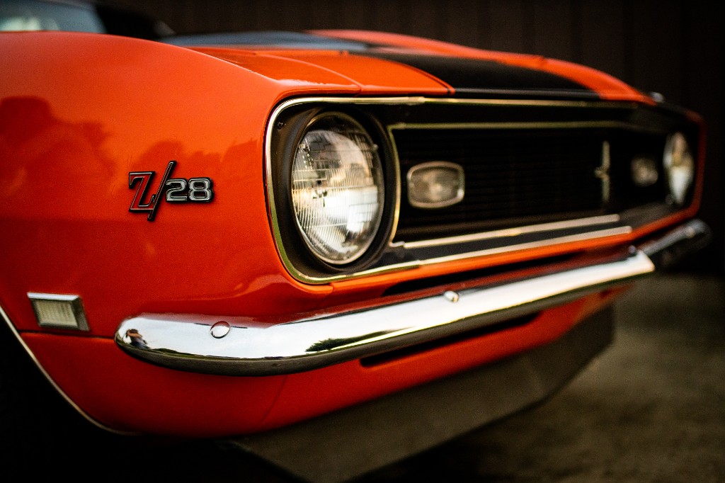 Front corner of orange Chevrolet Camaro Z/28 showing headlight, grille, and Z/28 emblem